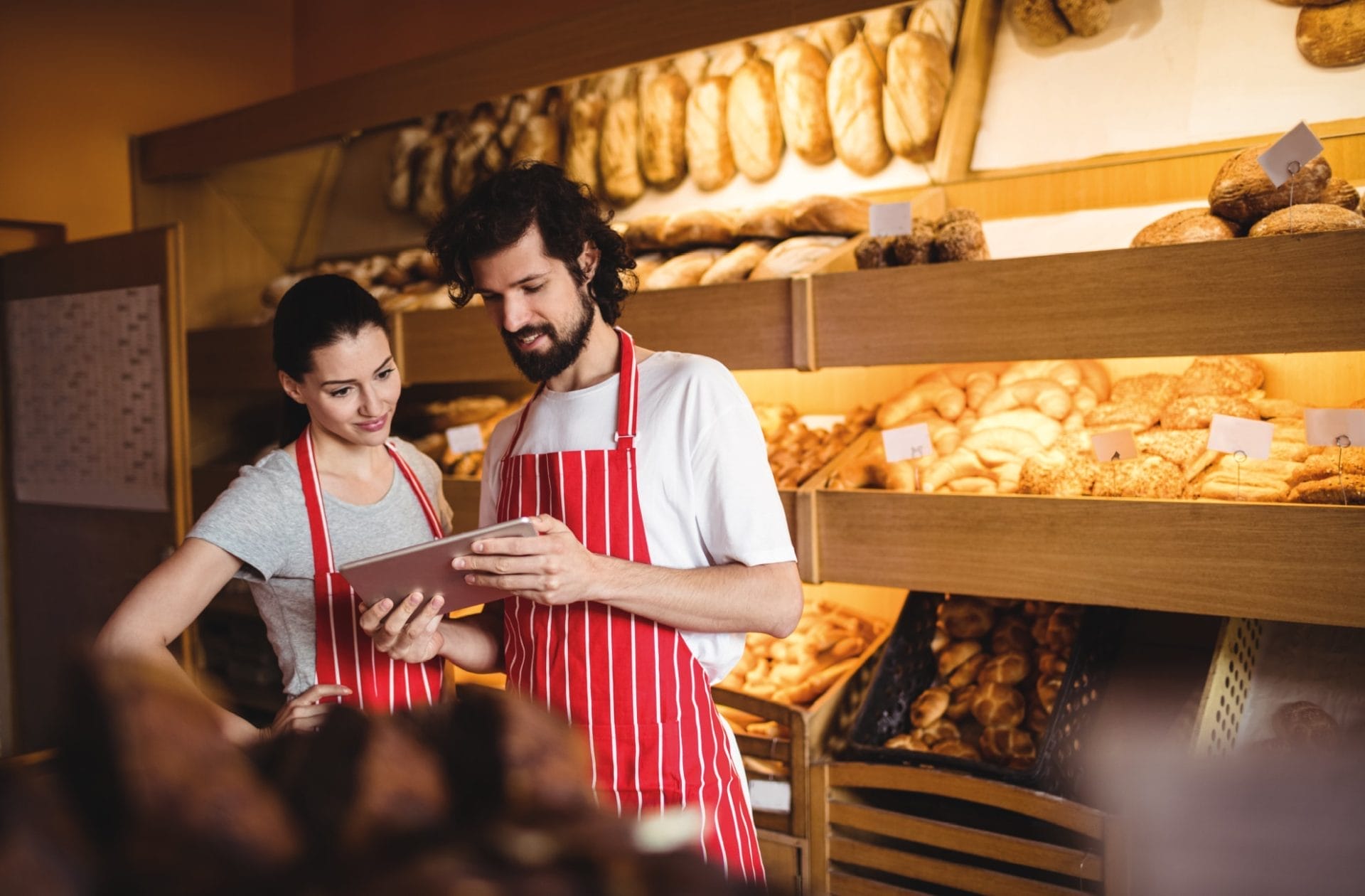 Zwei Bäckereiangestellte mit einem Tablet. 2 Bäckereiangestellte schauen hinter der Theke in ein Tablet.